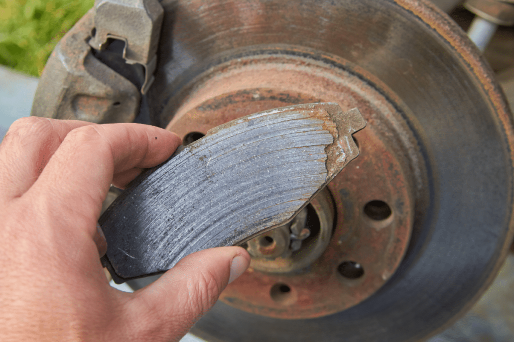 Brake pad replacement in Greer, SC, by Eastside Automotive. Image of a technician showing a worn-out brake pad needing replacement.