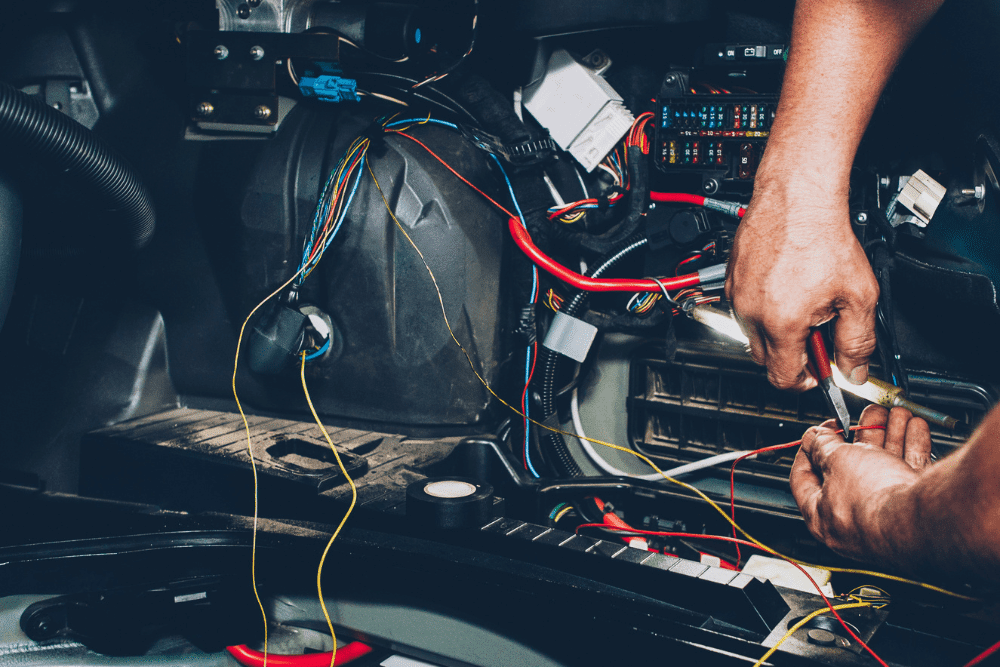 car electrical system repair, auto repair in Greer, SC at Eastside Automotive. A mechanic working on a vehicle's wiring system, carefully stripping and connecting wires near a fuse box.